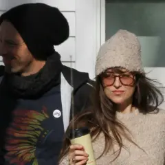 Dakota Johnson i Chris Martin w zimowych stylizacjach. Ona trzyma kubek, on ma na sobie koszulkę z motywem piór.