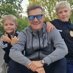 Marcin Mroczek z uśmiechem i dwoma synami, którzy przytulają się do niego.
