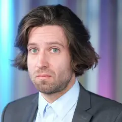 Michał Kempa w garniturze i jasnej koszuli, z burzą włosów i niebieskimi oczami.