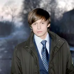 Piotr Ligienza, ubrany w elegancki garnitur i płaszcz, pozuje na tle mrocznego, zimowego krajobrazu. Może właśnie wraca do żony po długim dniu.