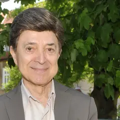 Uśmiechnięty Jerzy Połomski, w szarym garniturze i jasnej koszuli, na tle zieleni. Czyżby szukał partnera do wspólnego śpiewania?