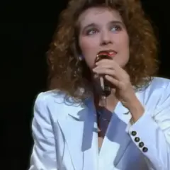 Celine Dion w białej marynarce śpiewa do mikrofonu, przypominając jej występ na Eurowizji.