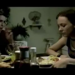Dwie kobiety siedzą przy stole, jedna z nich mówi, druga wygląda na zamyśloną, jakby czuła się **numb**.