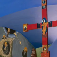 Czerwony krzyż z ikonami i malowidła ścienne przedstawiające sceny religijne, tworzące atmosferę sakralną.