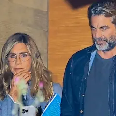 Jennifer Aniston z partnerem, w okularach, z telefonem i książką w ręku, obok mężczyzny z siwą brodą.
