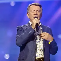Wojciech Gąsowski w niebieskiej marynarce i kwiecistej koszuli śpiewa na scenie.