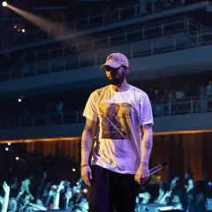 Eminem w czapce i białej koszulce z grafiką, na koncercie przed publicznością.