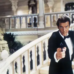 Roger Moore w smokingu z pistoletem, jakby szukał swojej żony w egzotycznym pałacu.