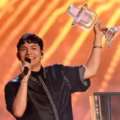 Szczęśliwy zwycięzca Eurowizji z pucharem w ręku, śpiewający na scenie.