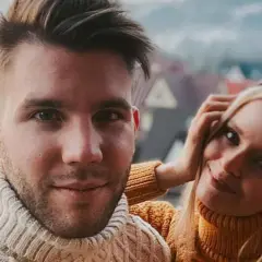 Olga Kalicka i jej partner w ciepłych swetrach, uśmiechnięci na tle górskiego krajobrazu.