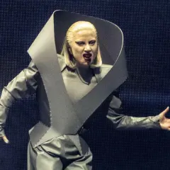 Lady Gaga w futurystycznym stroju na koncercie, z charakterystycznym kołnierzem i mocnym makijażem.