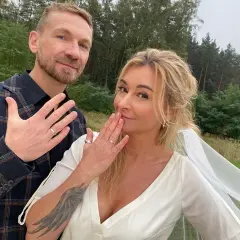 Martyna Wojciechowska i Kossakowski pokazują obrączki. Uśmiechnięci, w plenerze, świętują ważny moment.