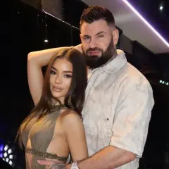 Wojtek Gola z dziewczyną, w eleganckich strojach, pozują do zdjęcia w nastrojowym oświetleniu.