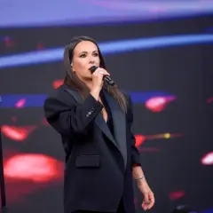Kasia Kowalska śpiewa na scenie, wykonując swoje utwory w eleganckiej czarnej marynarce.