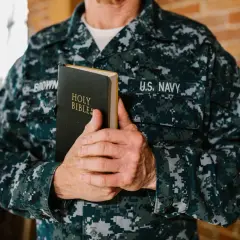 Marynarz w mundurze U.S. Navy trzyma Biblię. W jego dłoniach spoczywa księga, która może zawierać pieśń dawida, symbol wiary i nadziei.