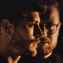Zbliżenie na twarze dwóch mężczyzn. Jeden z nich, Jakub Józef Orliński, patrzy w bok. Obok niego, w okularach, jego partner.