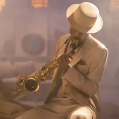 Mężczyzna w eleganckim, beżowym garniturze i kapeluszu gra na saksofonie, emanując prawdziwym jazzowy styl.