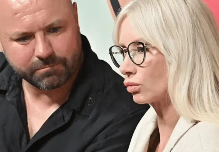 Piotr Domaniecki wiek nie jest widoczny, ale jego twarz jest skupiona. Obok niego siedzi kobieta w okularach.