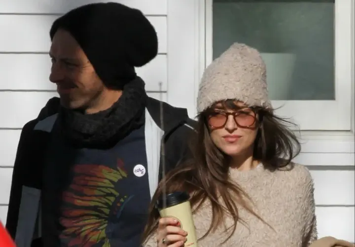 Dakota Johnson i Chris Martin w zimowych stylizacjach. Ona trzyma kubek, on ma na sobie koszulkę z motywem piór.