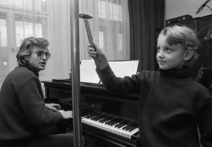 Zbigniew Wodecki gra na pianinie, a Paweł Wodecki trzyma młotek, jakby chciał uderzyć w klawisze.