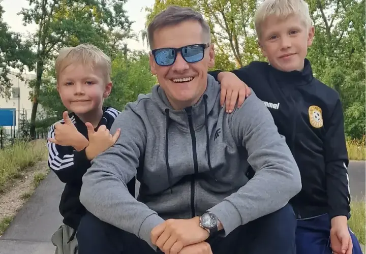 Marcin Mroczek z uśmiechem i dwoma synami, którzy przytulają się do niego.