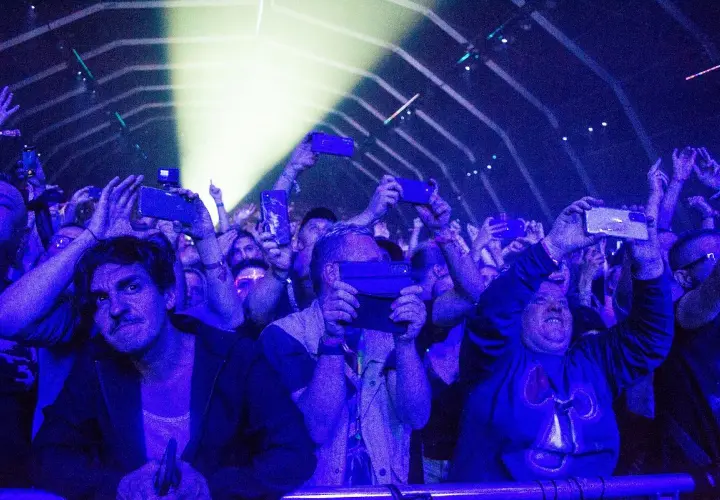 Tłum na fest festiwalu nagrywa koncert telefonami. Światła sceny oświetlają twarze ludzi.