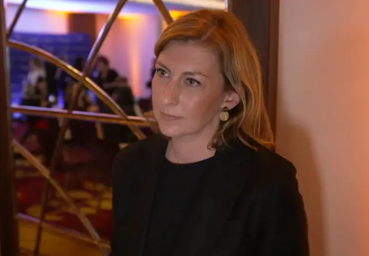 Olga Leonowicz, w wieku około 40 lat, w czarnej marynarce, z blond włosami i złotymi kolczykami, stoi przed lustrem.