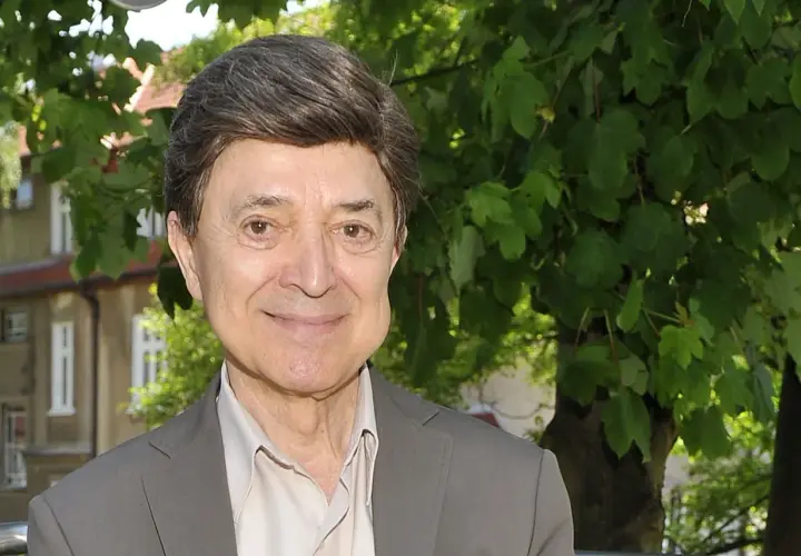Uśmiechnięty Jerzy Połomski, w szarym garniturze i jasnej koszuli, na tle zieleni. Czyżby szukał partnera do wspólnego śpiewania?