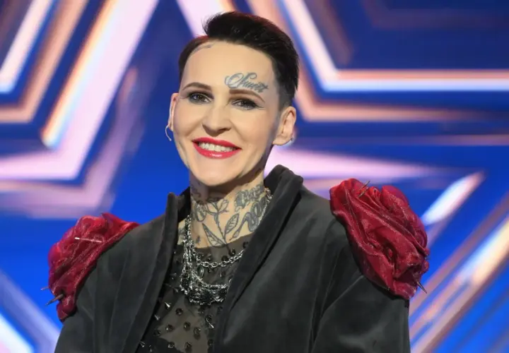 Agnieszka Chylińska z tatuażami na twarzy i szyi, w czarnej marynarce z czerwonymi ozdobami na ramionach.
