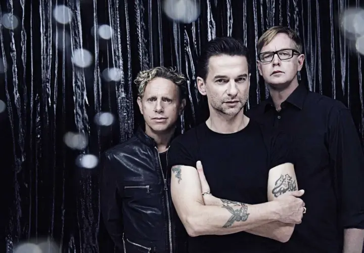Skład Depeche Mode: Martin Gore, Dave Gahan i Andy Fletcher pozują na tle błyszczącej, czarnej kurtyny.