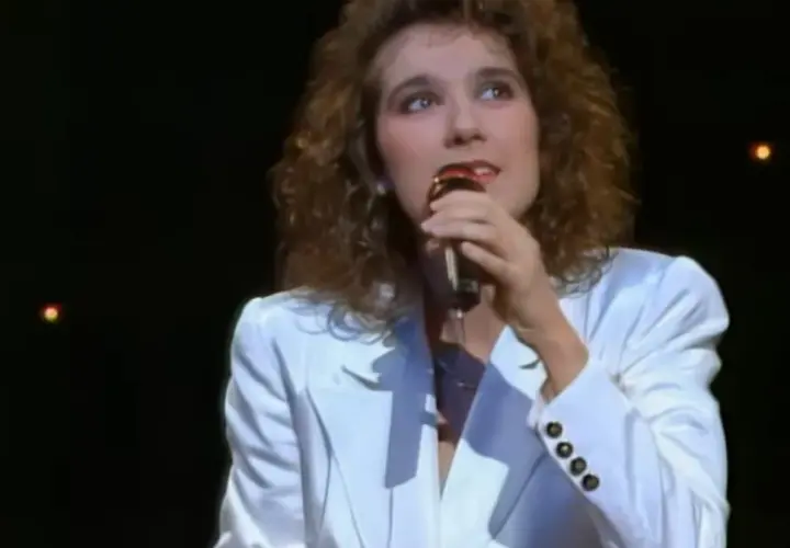Celine Dion w białej marynarce śpiewa do mikrofonu, przypominając jej występ na Eurowizji.