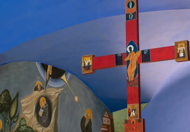 Czerwony krzyż z ikonami i malowidła ścienne przedstawiające sceny religijne, tworzące atmosferę sakralną.