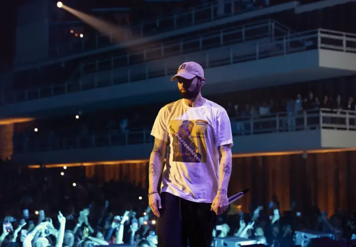 Eminem w czapce i białej koszulce z grafiką, na koncercie przed publicznością.