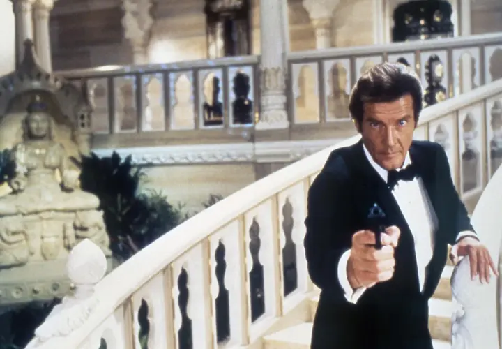 Roger Moore w smokingu z pistoletem, jakby szukał swojej żony w egzotycznym pałacu.