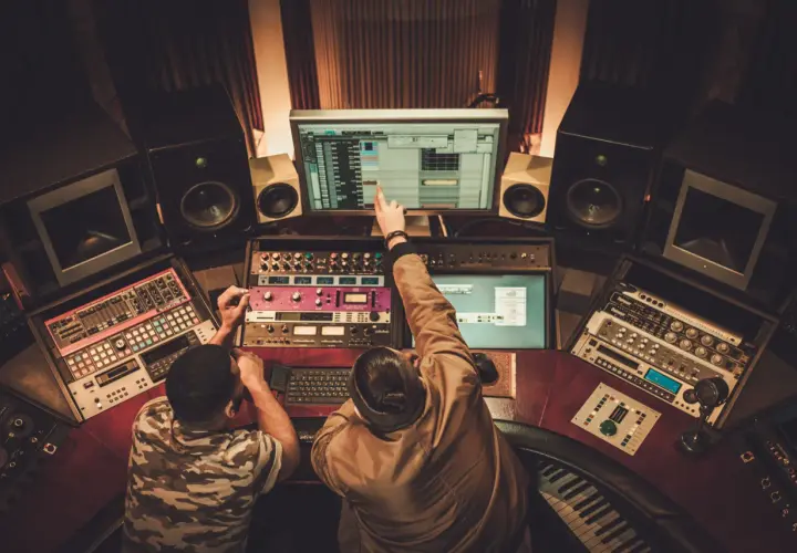 Dwóch producentów muzycznych w Polsce pracuje nad nowym hitem w studio nagraniowym, otoczeni sprzętem i monitorami.