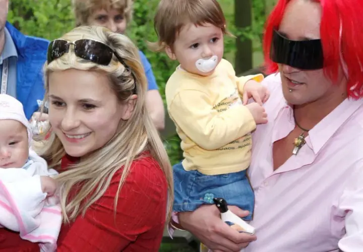 Uśmiechnięta kobieta z dzieckiem na rękach i mężczyzna z rudymi włosami trzymający drugie dziecko. To pola wiśniewska dzieci.
