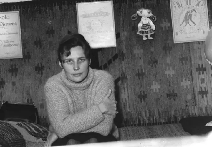Młoda kobieta w swetrze siedzi na tle gobelinu. Na ścianie wiszą dyplomy i lalka. Czy to Agnieszka Osiecka, której prawdziwe nazwisko brzmi...