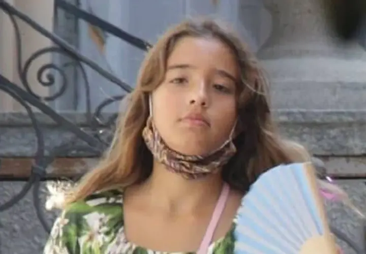 Léonie Cassel, z wachlarzem w ręku i maseczką na szyi, w kwiecistej sukience.