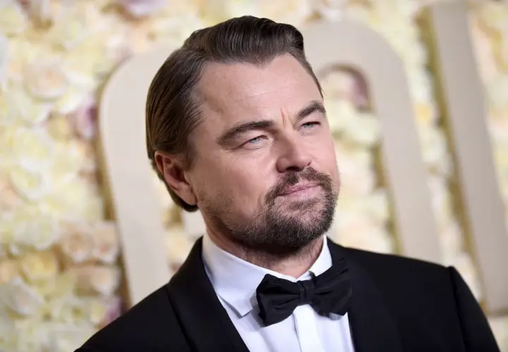 Leonardo DiCaprio wiek: doświadczony aktor w czarnym smokingu z muszką, z siwiejącymi włosami i kilkudniowym zarostem.