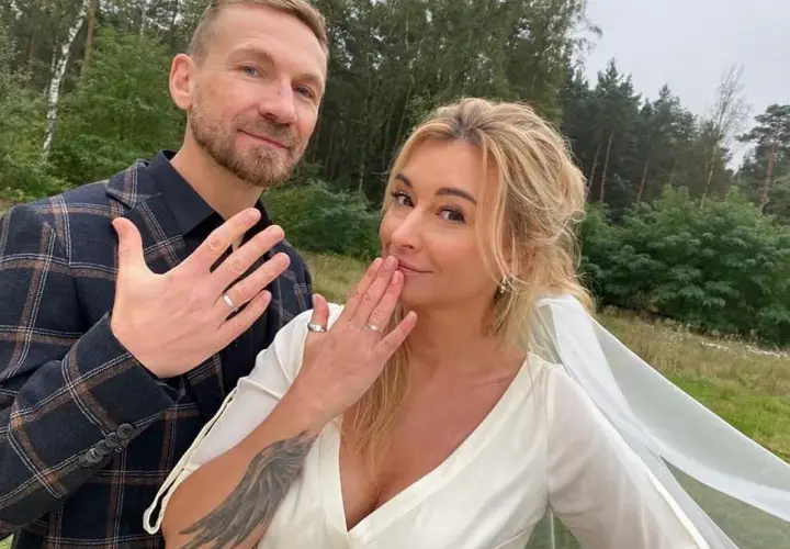 Martyna Wojciechowska i Kossakowski pokazują obrączki. Uśmiechnięci, w plenerze, świętują ważny moment.
