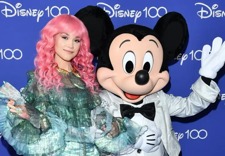 Dziewczyna z różowymi włosami i Myszka Miki pozdrawiają na tle napisu "Disney 100". Może to zapowiedź nowych piosenek Disneya?