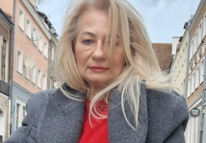 Szafiarka Dorka, ile ma lat? Kobieta w szarym płaszczu i czerwonym swetrze na tle kamienic.