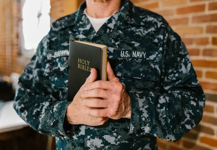 Marynarz w mundurze U.S. Navy trzyma Biblię. W jego dłoniach spoczywa księga, która może zawierać pieśń dawida, symbol wiary i nadziei.