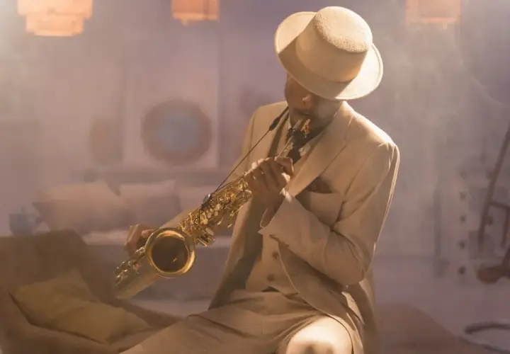 Mężczyzna w eleganckim, beżowym garniturze i kapeluszu gra na saksofonie, emanując prawdziwym jazzowy styl.