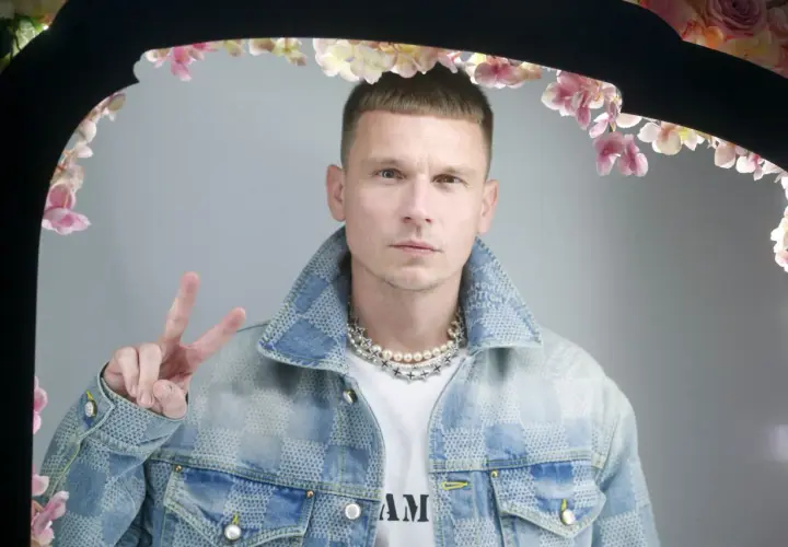 Bart Pniewski, młody mężczyzna w jeansowej kurtce, pozuje z uniesionym znakiem pokoju.