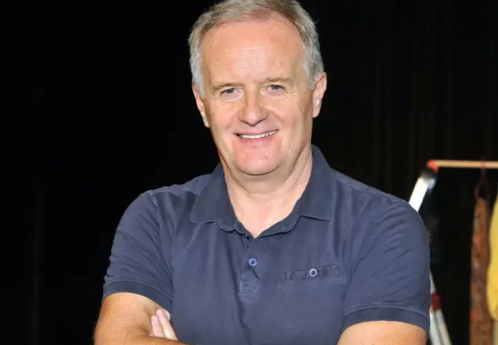 Aleksander Mikołajczak w granatowej koszulce polo, uśmiechnięty, z rękami skrzyżowanymi na piersi.
