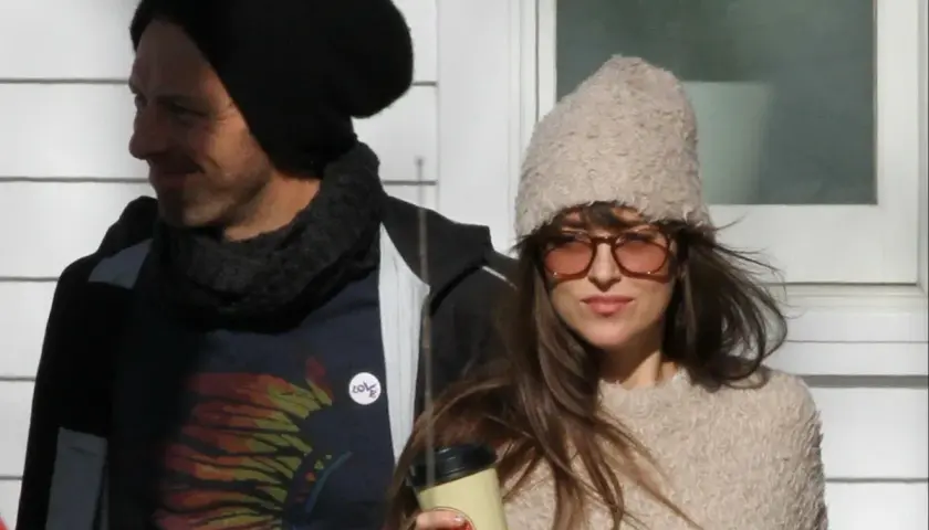 Dakota Johnson i Chris Martin w zimowych stylizacjach. Ona trzyma kubek, on ma na sobie koszulkę z motywem piór.