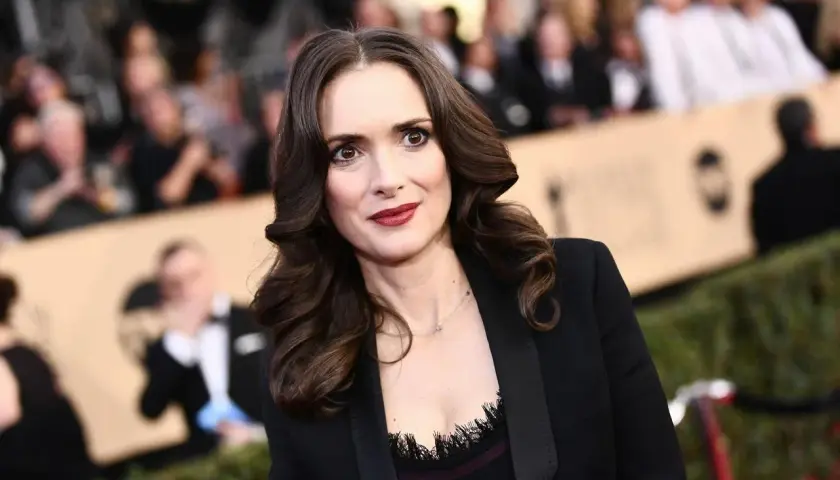 Winona Ryder w czarnej marynarce, z burzą brązowych włosów. Wygląda jakby opowiadała o swoich dzieciach.