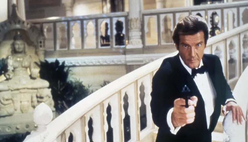 Roger Moore w smokingu z pistoletem, jakby szukał swojej żony w egzotycznym pałacu.