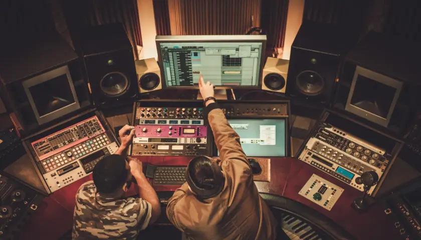 Dwóch producentów muzycznych w Polsce pracuje nad nowym hitem w studio nagraniowym, otoczeni sprzętem i monitorami.